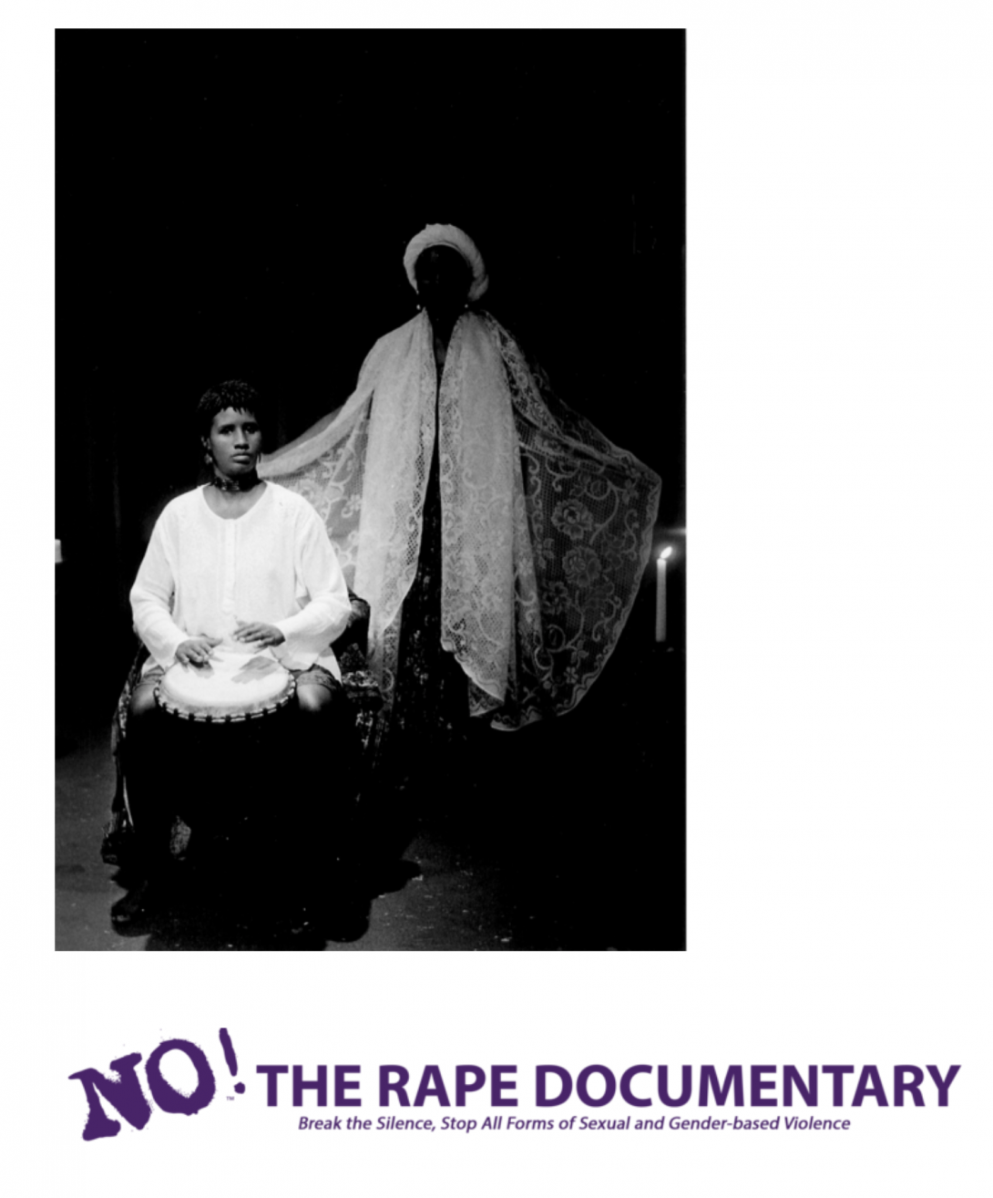 A black and white, still image from the film showing a Black person in a white tunic sitting and playing a drum with their hands, and another person in a lacy white cape standing behind them with their arms partially outstretched.