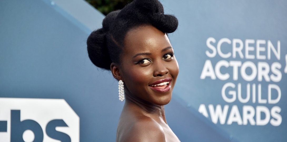 Lupita Nyonga at Screen Actors Guild Awards red carpet with 1940s pin up style hair.