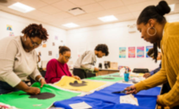 Black women gathered around a table stitching quilt squares
