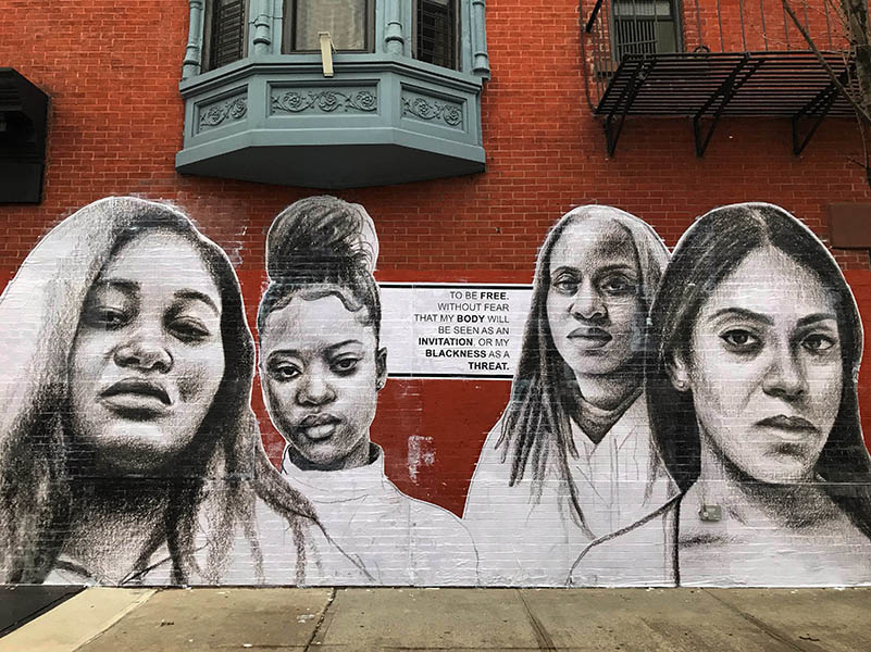 faces of 4 Black women painted in Black and white in a red building wall