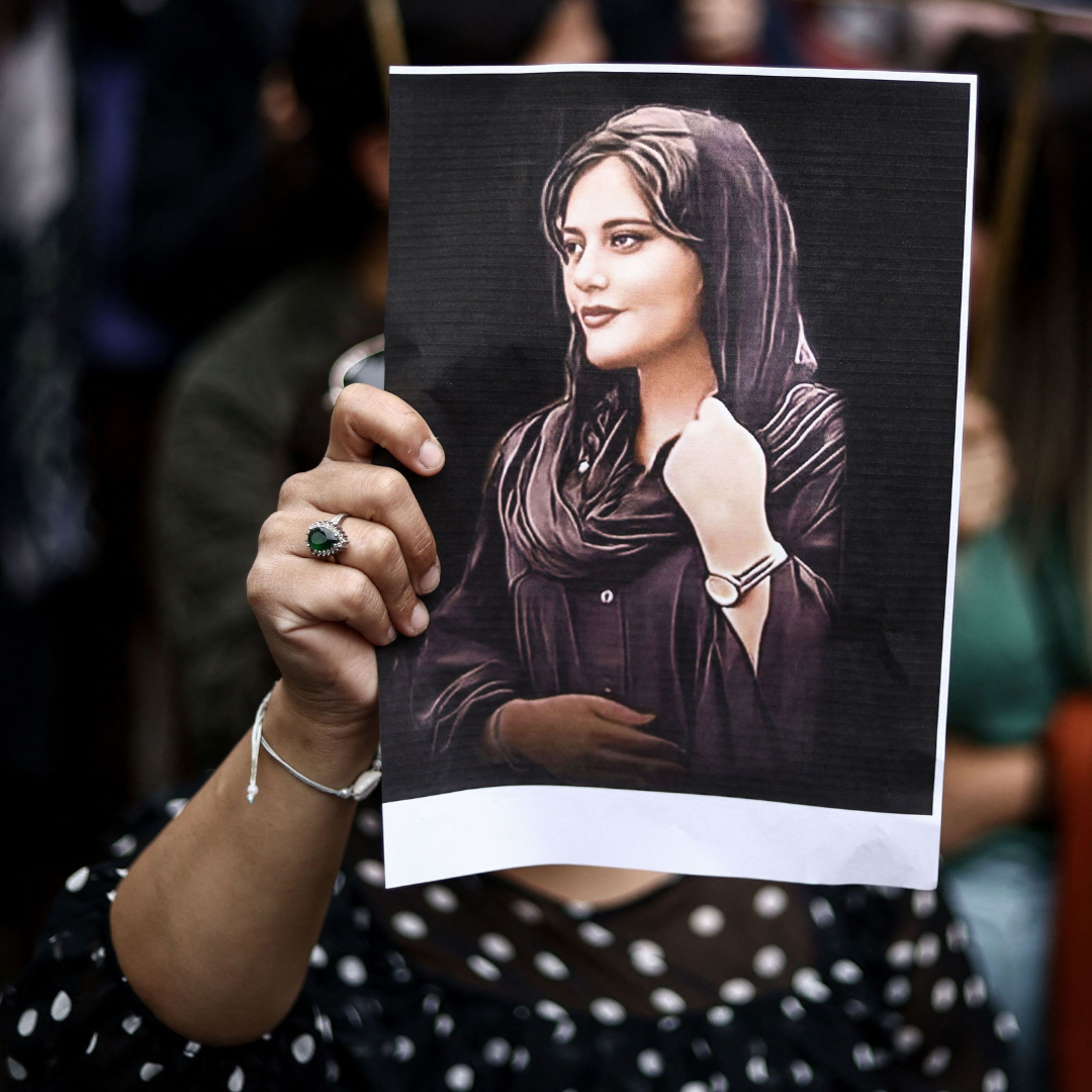 A person holds up a photo of Mahsa Amini at an outdoor demonstration. Photo credit: CNN.com.