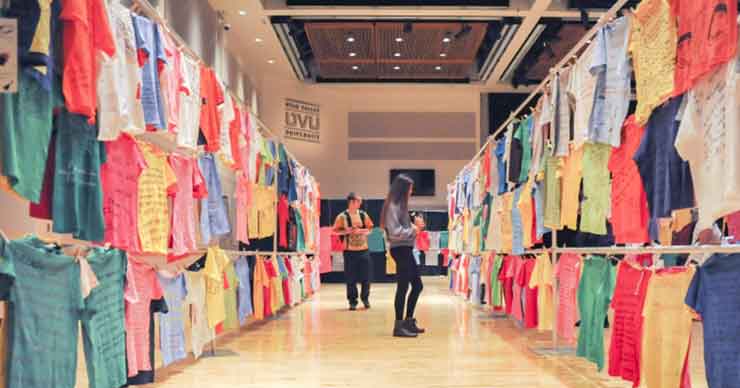 Two people stand in a gallery of shirts hanging on clotheslines.
